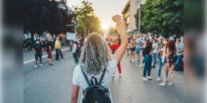 Manifestation d'un mouvement féministe avec une jeune femme levant le poing, entourée de pancartes revendiquant l'égalité des genres dans la société