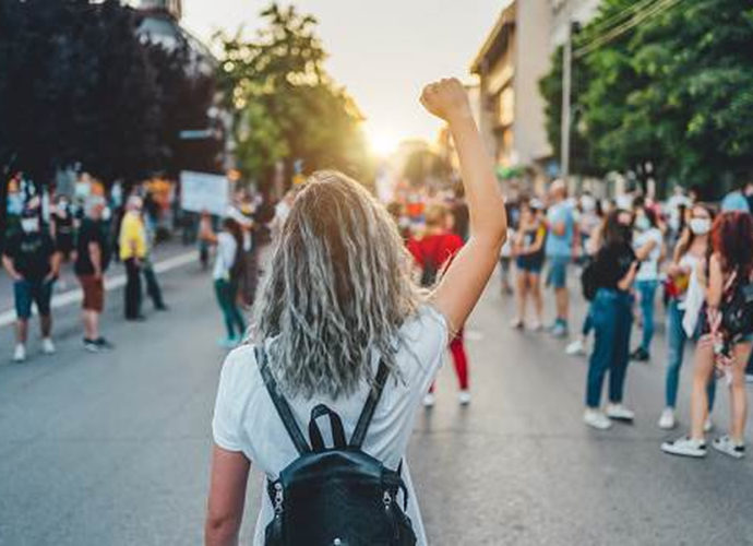 Manifestation d'un mouvement féministe avec une jeune femme levant le poing, entourée de pancartes revendiquant l'égalité des genres dans la société