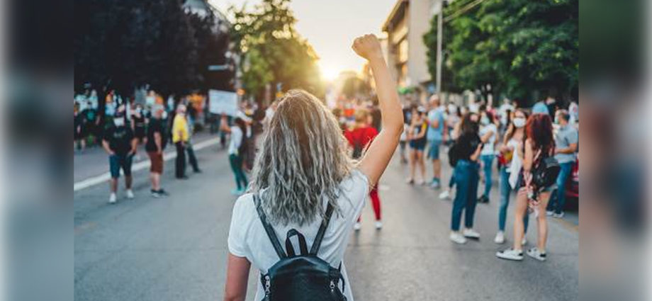 Manifestation d'un mouvement féministe avec une jeune femme levant le poing, entourée de pancartes revendiquant l'égalité des genres dans la société